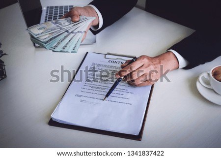 Loan agreement, Borrow money, corruption concept,
Male holding pen pointing contract application and give dollar bank.