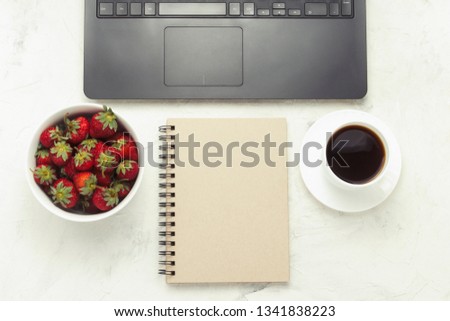 Workplace. Laptop, notebook, cup of coffee, in a bowl of strawberries. Top View, flat lay.