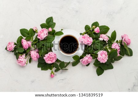 White cup with black coffee and pink roses on a light stone background. Flat lay, top view