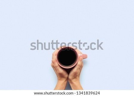 Two hands holding a cup with hot coffee on a blue background. Breakfast concept with coffee or tea. Good morning, night, insomnia. Flat lay, top view