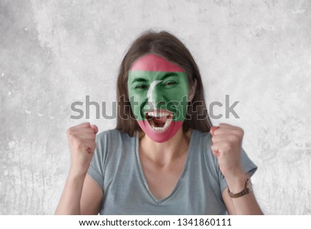 Young woman with painted flag of Maldives and open mouth looking energetic with fists up