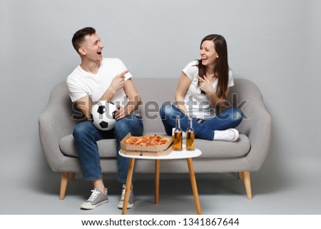 Laughing couple woman man football fans cheer up support favorite team with soccer ball pointing index fingers isolated on grey wall background. People emotions sport family leisure lifestyle concept