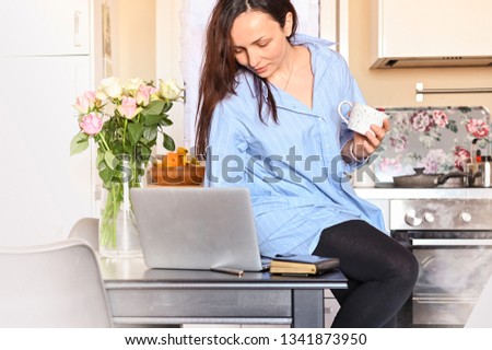 Girl holding a notepad and coffee sits at a table with a computer. Work at home and freelance. Cozy home compbueter and flowers on the table. Business lady at home. Free space for text. Photo toning.
