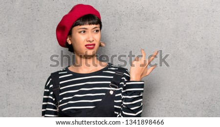 Young woman with beret surprised and shocked while looking right over textured wall
