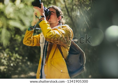 Portrait of an explorer taking photos of nature standing in a forest. Photographer wearing jacket and backpack doing nature photography.