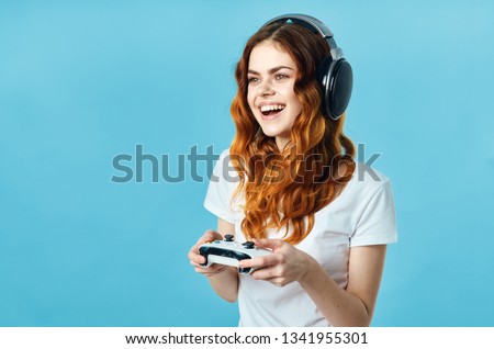 Cheerful woman Gamer in headphones with a gamepad in the hands of the gaming console blue background