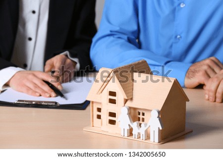 Real estate agent working with client at table, focus on house and family figures. Home insurance