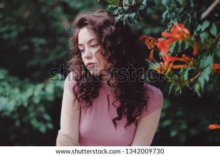 Portrait of young caucasian woman with curly hair and freckles in the garden.
