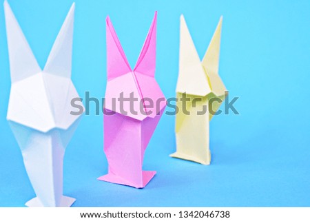 Origami bunnies folded from pastel paper stand on a blue surface - Concept with origami for Easter with strong colors
