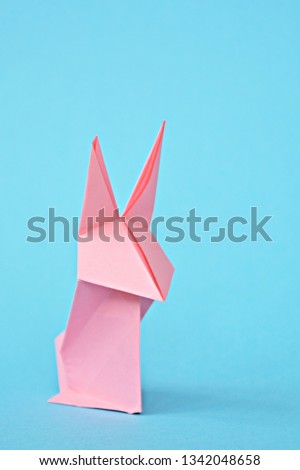 A origami bunny folded from pastel paper stands on a blue base - concept with origami and place for text or other elements for Easter