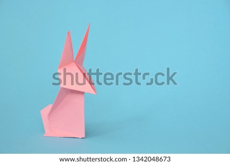A origami bunny folded from pastel paper stands on a blue base - concept with origami and place for text or other elements for Easter