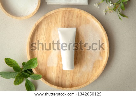 Top down view of Organic gentle skincare product cleanser white tube with a blank label on a wooden plate decoration with leaves and white flower on grey background. Royalty-Free Stock Photo #1342050125