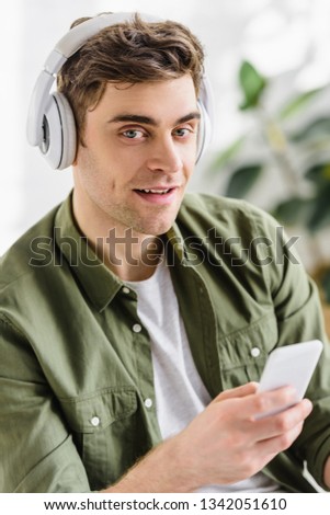 handsome businessman in green shirt and headphones holding smartphone in office