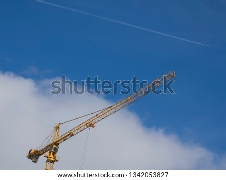View for Working yellow construction crane against blue sky and the plane in the background