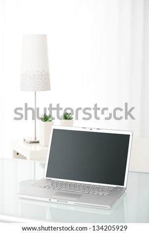 Laptop computer with screen visible on table in bright room, still-life picture.