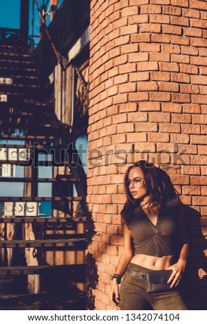 Young brunette girl in black standing outside and watching the sunset in the city, the sun shines brightly, fashionable clothes on a girl, hipster style,, tattoo, street photo, mood, freedom, Bali