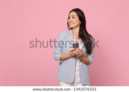 Smiling young woman in striped jacket looking aside using mobile phone, typing sms message isolated on pink pastel background in studio. People sincere emotions, lifestyle concept. Mock up copy space
