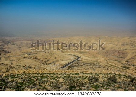 panoramic desert scenery landscape in Jordan holy mountain Nebo aerial photography with lonaly narrow curved road through dunes and horizontal board between foggy ground and blue sky, copy space