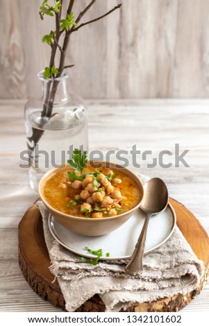 Cooked Chickpeas with stock served on a ceramic bowl with parsley, red peppers and seed bread over linen and wooden surface