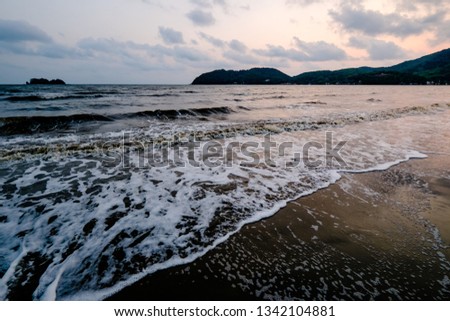 A golden light on Chanthaburi beach, Thailand. A sunset seascape photo. Motion of wave pass through sand and a leaf. A beautiful outdoor sea for holiday or traveling.