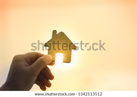 Left hand holding house shape figure on sunrise or sunset background with copy space. Business, financial, home mortgage, and housing concept