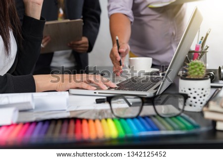 Designer Young asian using graphics tablet while working with computer at studio or office,Graphic design and color swatches and pens on a desk warm colours sun light.