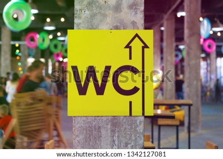 toilet pointer sign hanging on a concrete pillar