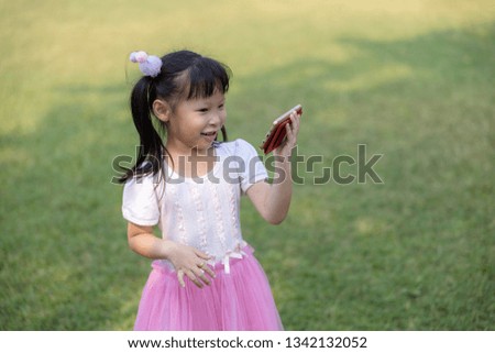 children thai girl on pink dress standing are touching  watching cartoon movies on smartphone with high-speed 4G WI-FI system in the garden