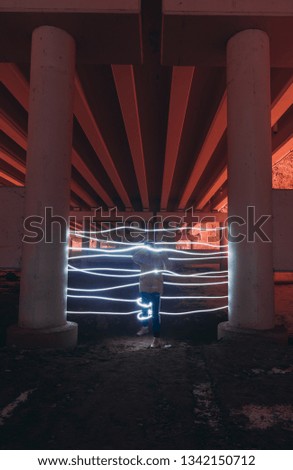 A person cannot pass through a neon gate painted with light at night under a bridge