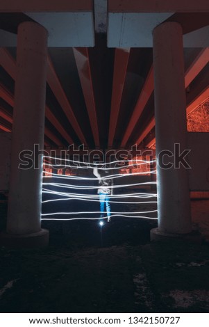 A person cannot pass through a neon gate painted with light at night under a bridge