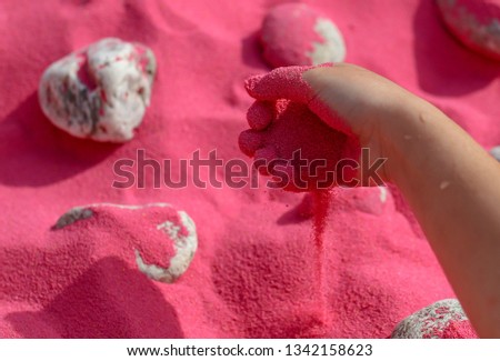 The child plays with his hands in the pink sand .