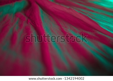 Soft focus, very shallow depth of field abstract picture of a wrinkled bed sheet lit by hot pink and bright teal lights.