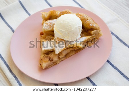 Slice of home-baked apple pie with ice cream on pink plate, side view. Closeup.