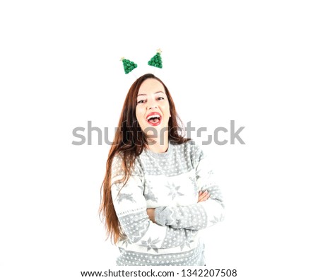 Excited young woman smiling while wearing a jumper and a headband with green trees on it against a white background