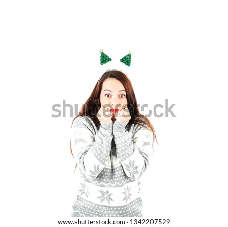 Excited young woman opening her eyes while wearing a jumper and a headband with green trees on it against a white background