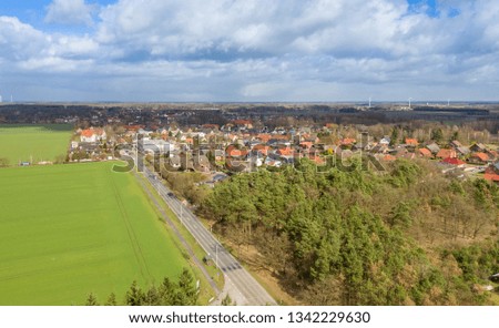 Aerial view of the entrance of a German small town with a country road between fields and woods for the development of the village, drone flight
