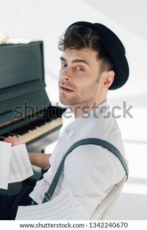 selective focus of handsome musician sitting by piano and looking at camera 
