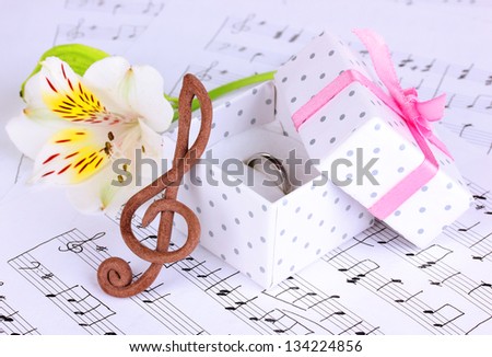 Treble clef, flower and box holding wedding ring on musical background