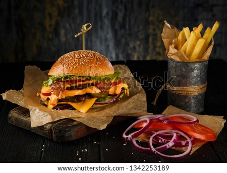 Cheeseburger and french fries on wooden table on dark background.