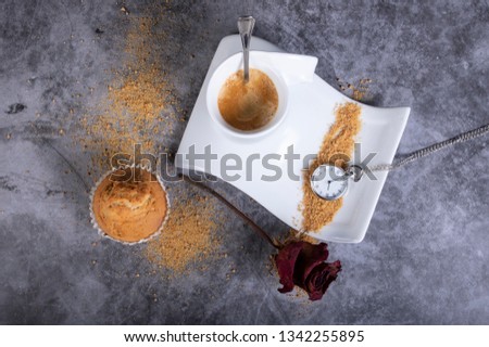 White porcelain coffee cup with brown sugar, cupcake, sugar bowl, rose and pocket watch that indicates that it is time to have a hot coffee with foam.