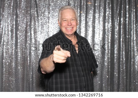 Man in a Photo Booth. A man smiles and poses in a Photo Booth with silver sequin curtains. Photo Booths are fun for all guest. 
