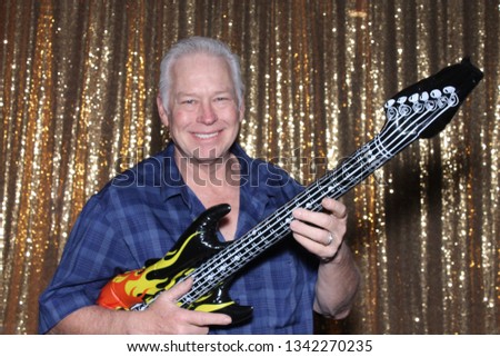 Man in a Photo Booth. A man smiles and poses with an inflatable guitar in a Photo Booth. Photo Booths are fun for all guest. 