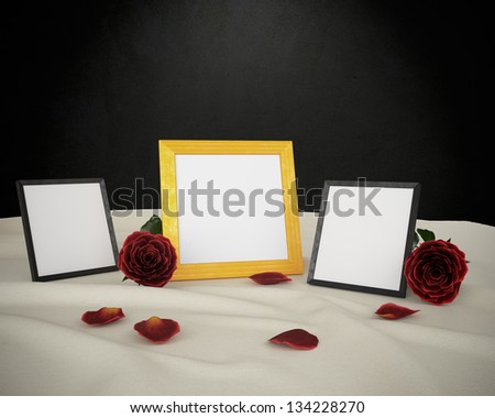 One golden and two black photo frames and roses on a table