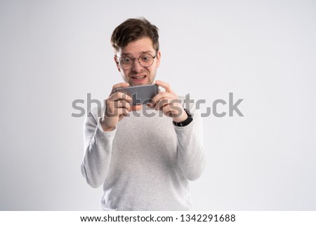 Portrait of an excited young man in white t-shirt playing games on mobile phone isolated over white background