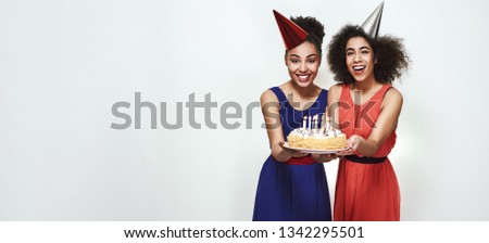 Time to make a wish! Wide photo of happy young afro american women in party hats holding a cake with candles while celebrating birthday