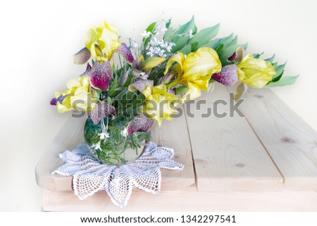 Still life with yellow irises in a glass vase on a table on a white background