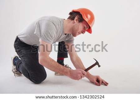 Careful with instrument. Man in casual clothes and orange colored hard hat have some work using hammer. White background.