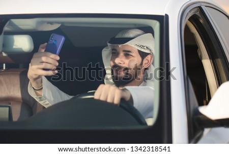 Arab man taking a selfie photo while he drive the car. Arabic man enjoy his new car.