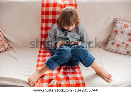A little boy plays in the phone, looks cartoon. Down syndrome. Baby in the smartphone. Play in social networks. Children at home.