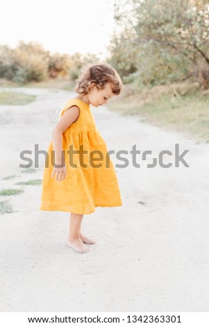 Little girl wearing mustard linen dress standing on coutry road. Summer vacation. Lifestyle photography